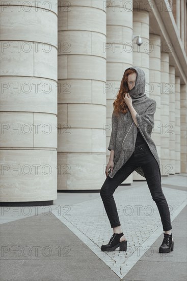 Caucasian woman hiding face behind hood near pillars