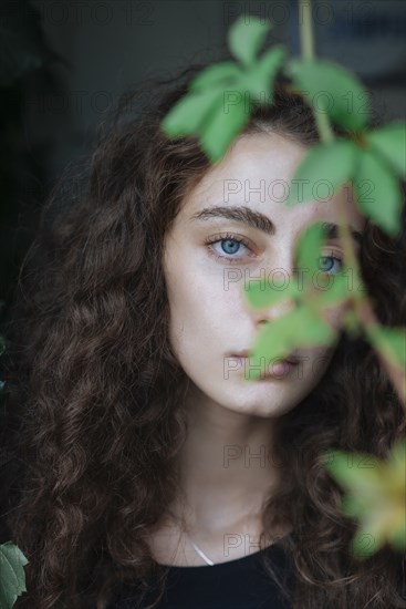 Portrait of serious Caucasian woman behind leaves