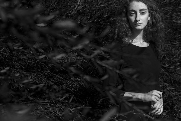 Serious Caucasian woman standing behind branches