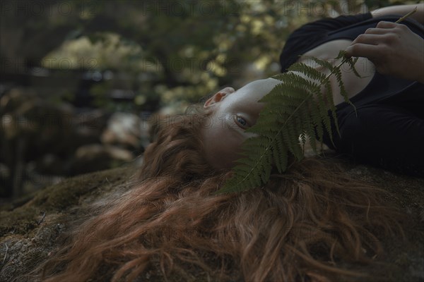 Caucasian woman with red hair hiding face behind leaf