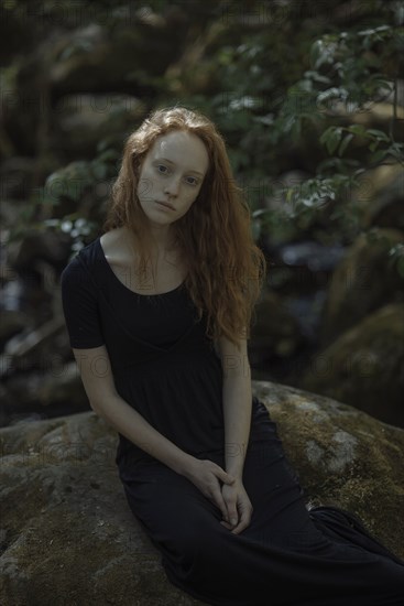 Serious Caucasian woman sitting on rock