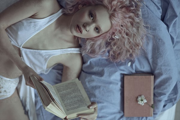 Caucasian woman laying on bed in underwear reading book