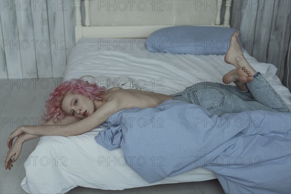 Topless Caucasian woman laying on bed wearing jeans