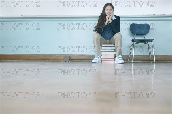 Teenage girl sitting on stack of books