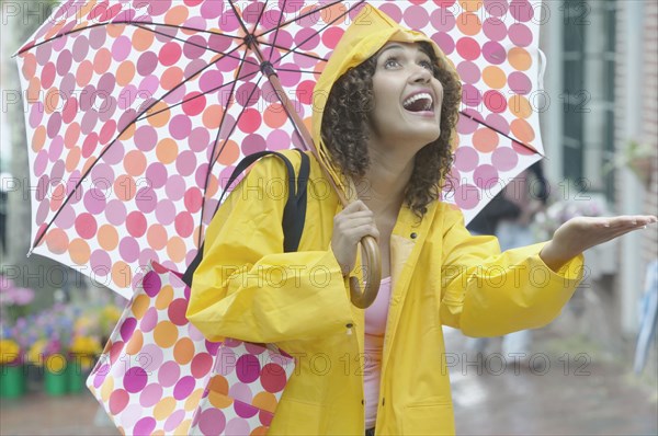 Hispanic woman in raincoat with umbrella checking for rain