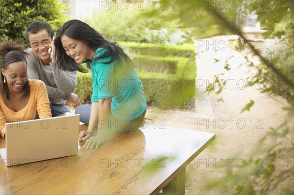 Three friends using laptop outdoors