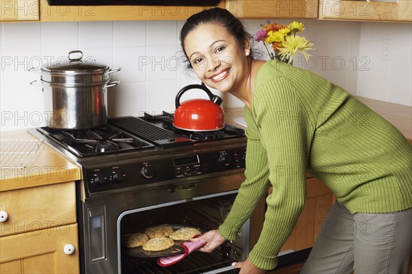 Young woman taking food out of the oven