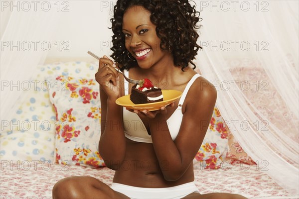 African woman eating cake on bed