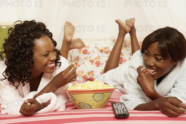 Two African women eating popcorn on bed