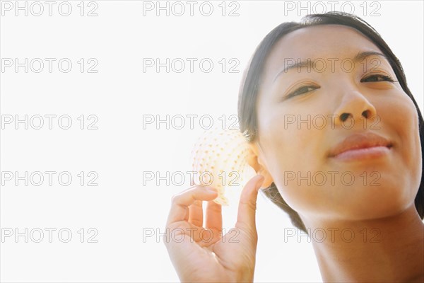 Asian woman listening to seashell