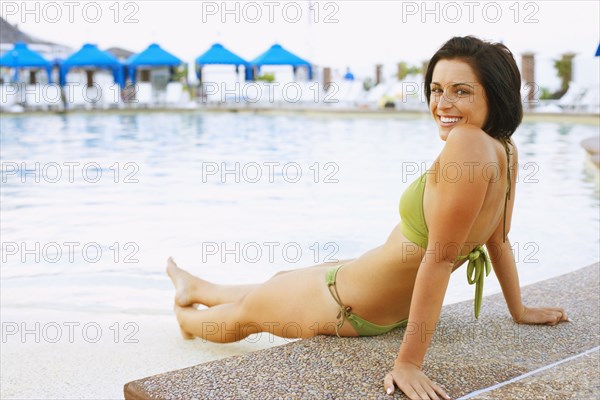Young woman sitting next to swimming pool