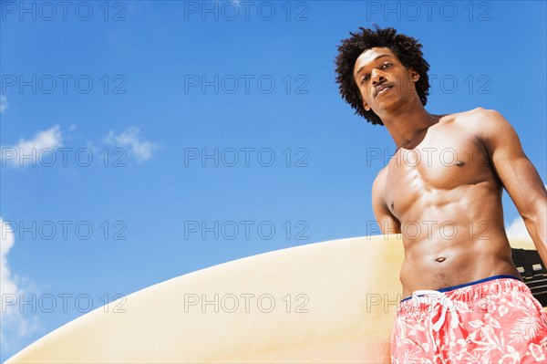 Serious African man holding surfboard