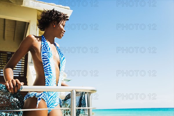 African woman in bathing suit on balcony looking at ocean