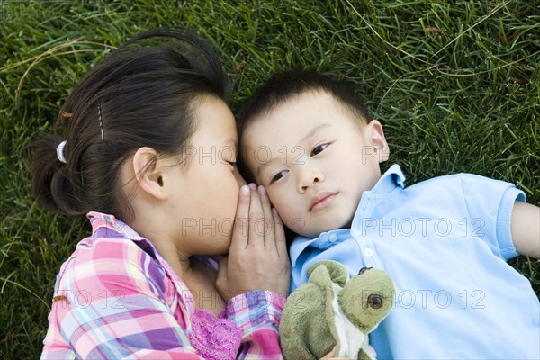 Chinese girl laying in grass and whispering to brother