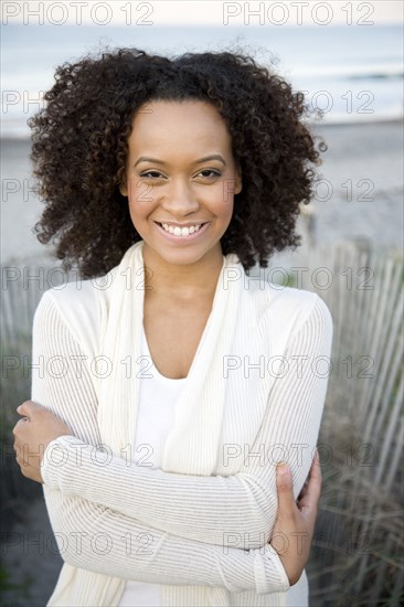 Smiling Hispanic woman at beach with arms crossed