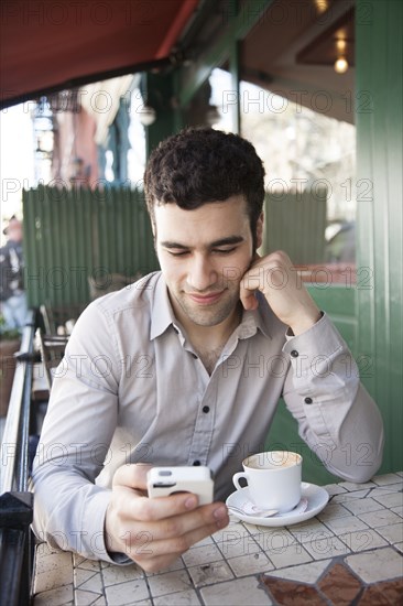 Hispanic man using cell phone at sidewalk cafe