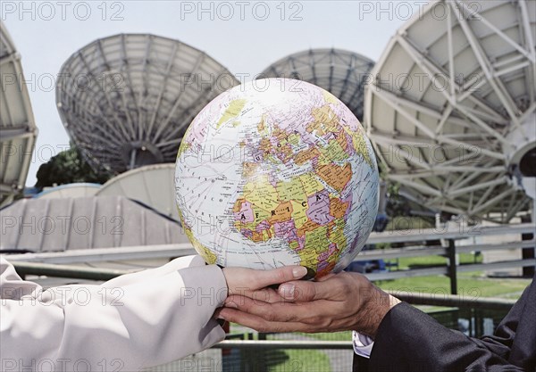 Businesspeople holding globe in front of satellite dishes