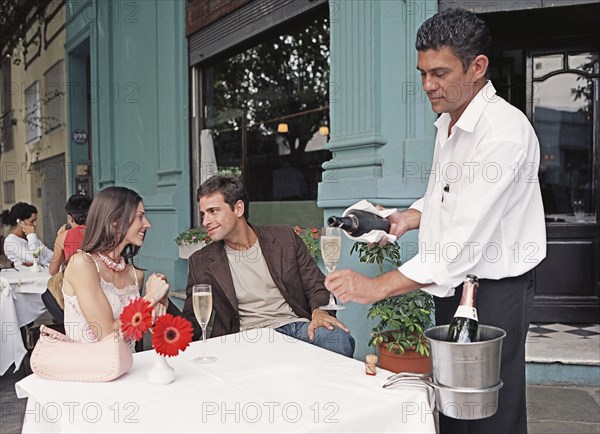 Hispanic couple having champagne at outdoor cafe