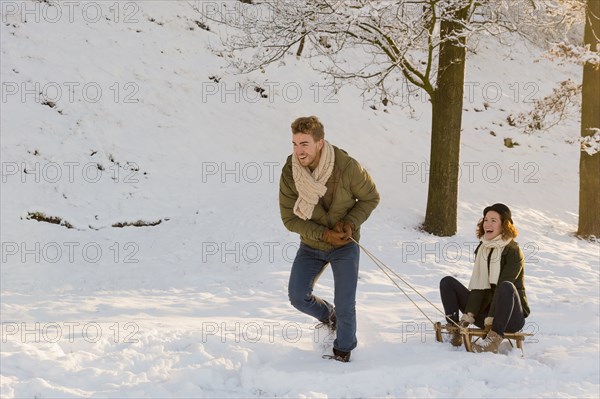 Caucasian man pulling girlfriend on sled in snow