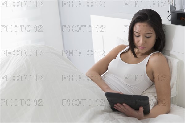 Mixed race woman using tablet computer in bed