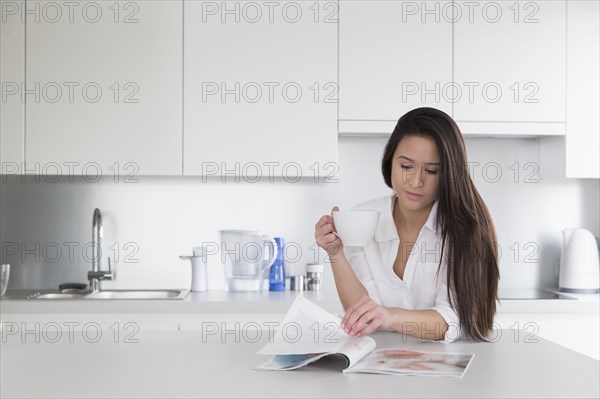 Mixed race woman reading magazine in kitchen