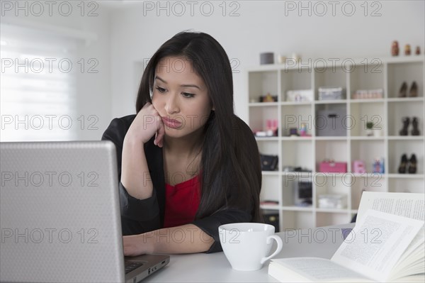 Bored mixed race businesswoman using laptop