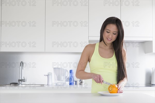 Mixed race woman slicing fruit in kitchen