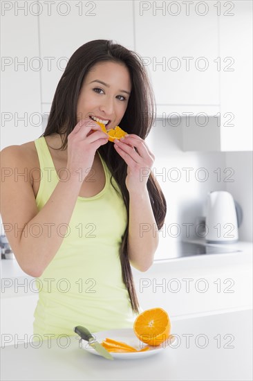 Mixed race woman eating fruit in kitchen