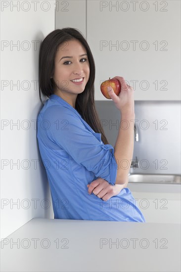 Mixed race woman eating fruit in kitchen