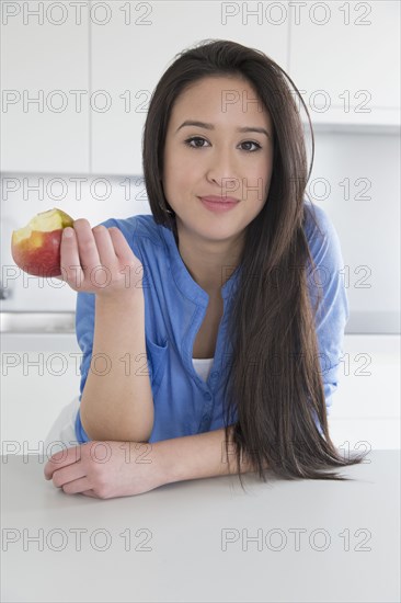 Mixed race woman eating fruit in kitchen