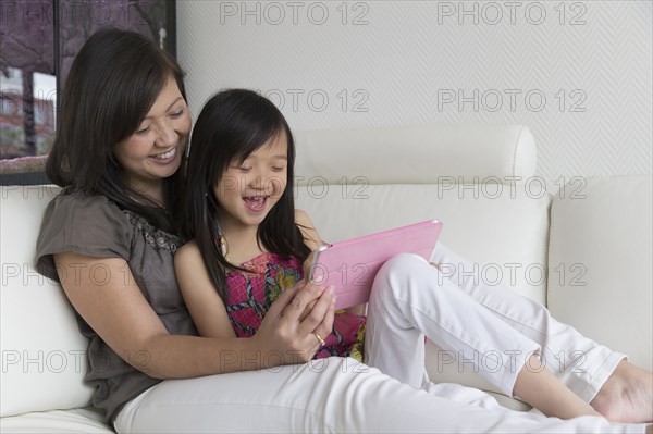 Asian mother and daughter using digital tablet on sofa