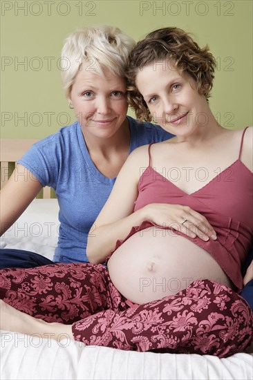 Caucasian pregnant lesbian couple relaxing on bed