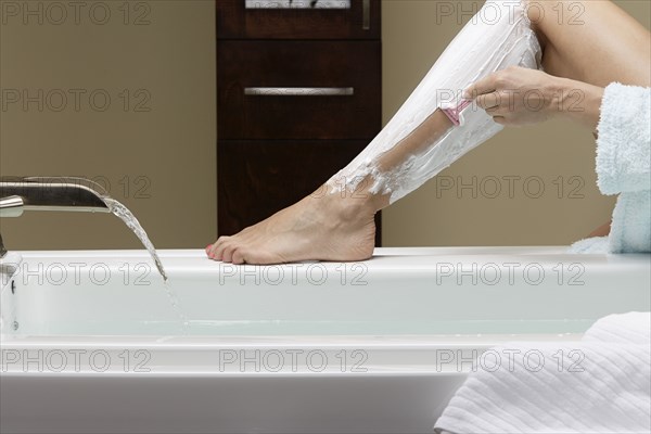 Caucasian woman shaving her legs at bathtub