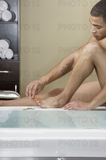 Mixed race man filing his toenails at bathtub