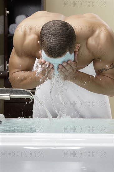 Mixed race man washing off facial mask in bath