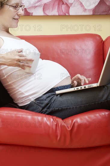 Caucasian pregnant woman using laptop on sofa