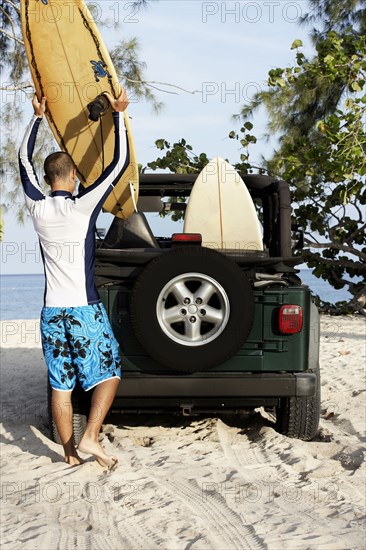 Mixed race man loading surfboards into 4x4 on beach