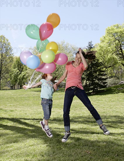 Mixed race mother and daughter holding balloons in park