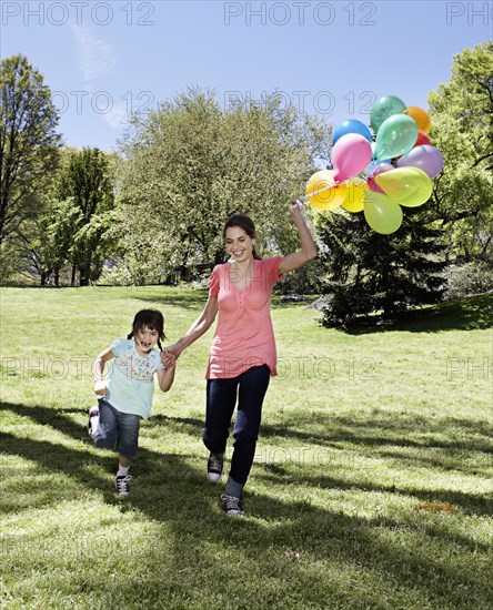 Mixed race mother and daughter holding balloons in park