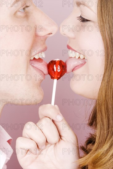 Caucasian couple licking lollipop