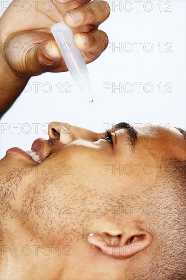 Mixed race man putting in eye drops