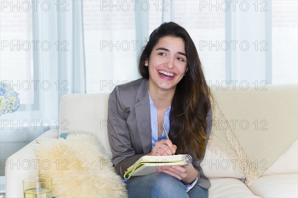 Hispanic woman taking notes on sofa