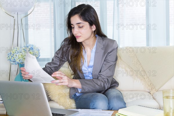 Hispanic woman using laptop on sofa