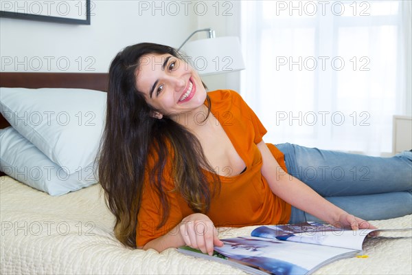Hispanic woman reading magazine on bed