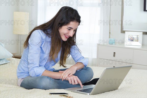 Hispanic woman using laptop on bed