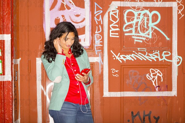 Mixed race woman listening to headphones against graffiti wall