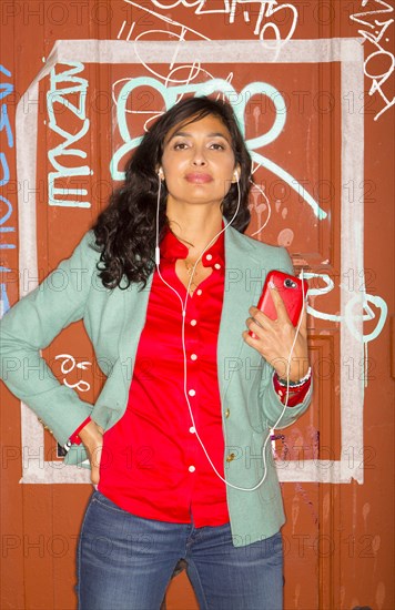 Mixed race woman listening to headphones against graffiti wall