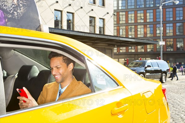 Mixed race businessman using cell phone in taxi