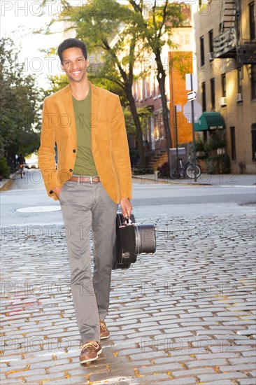 Mixed race man carrying guitar on city street