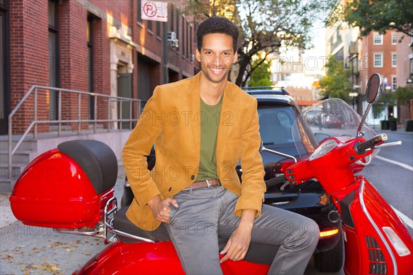 Mixed race man sitting on scooter on city street